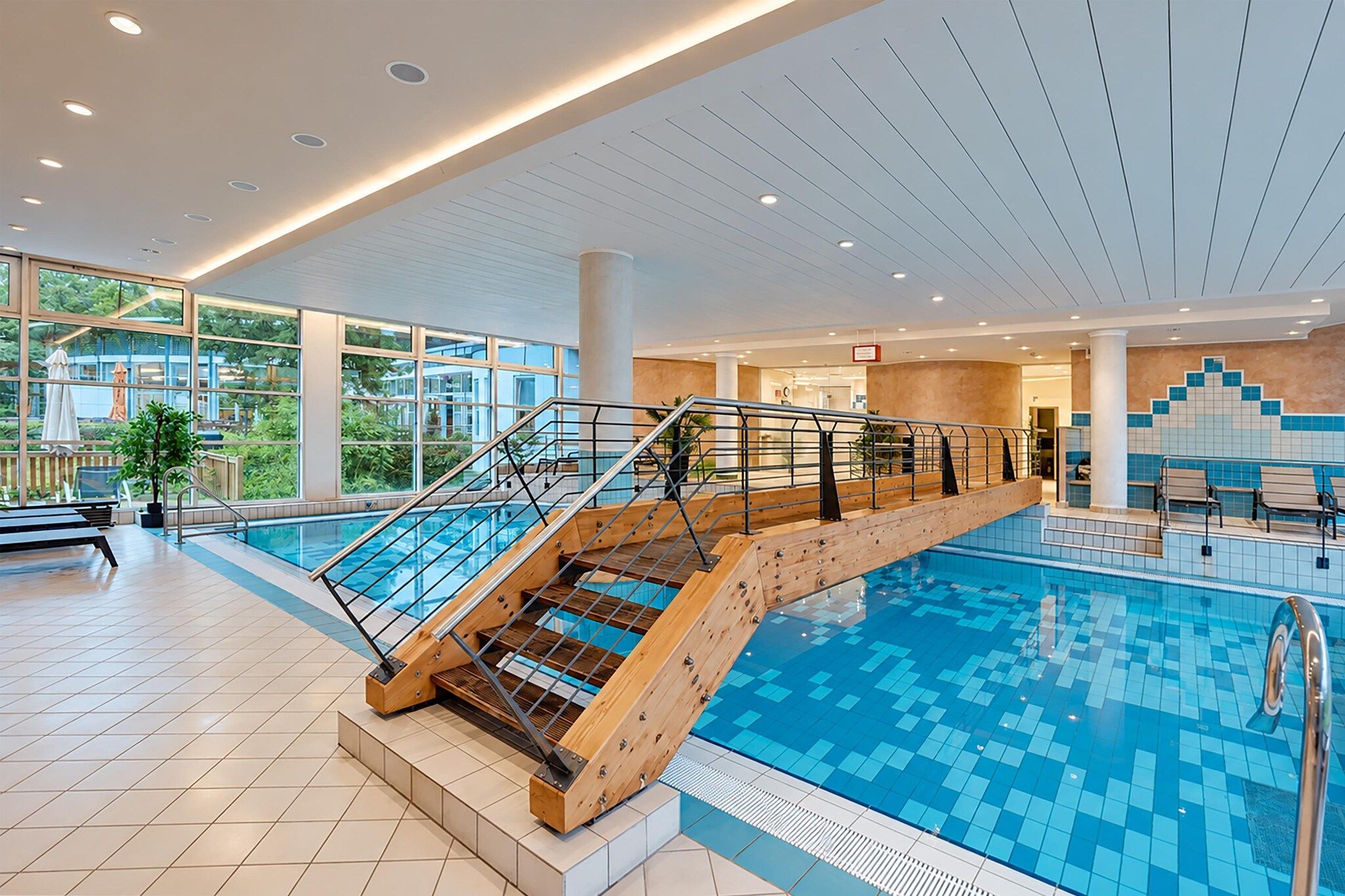 Una piscina interna con una scala in legno e ringhiere in vetro.