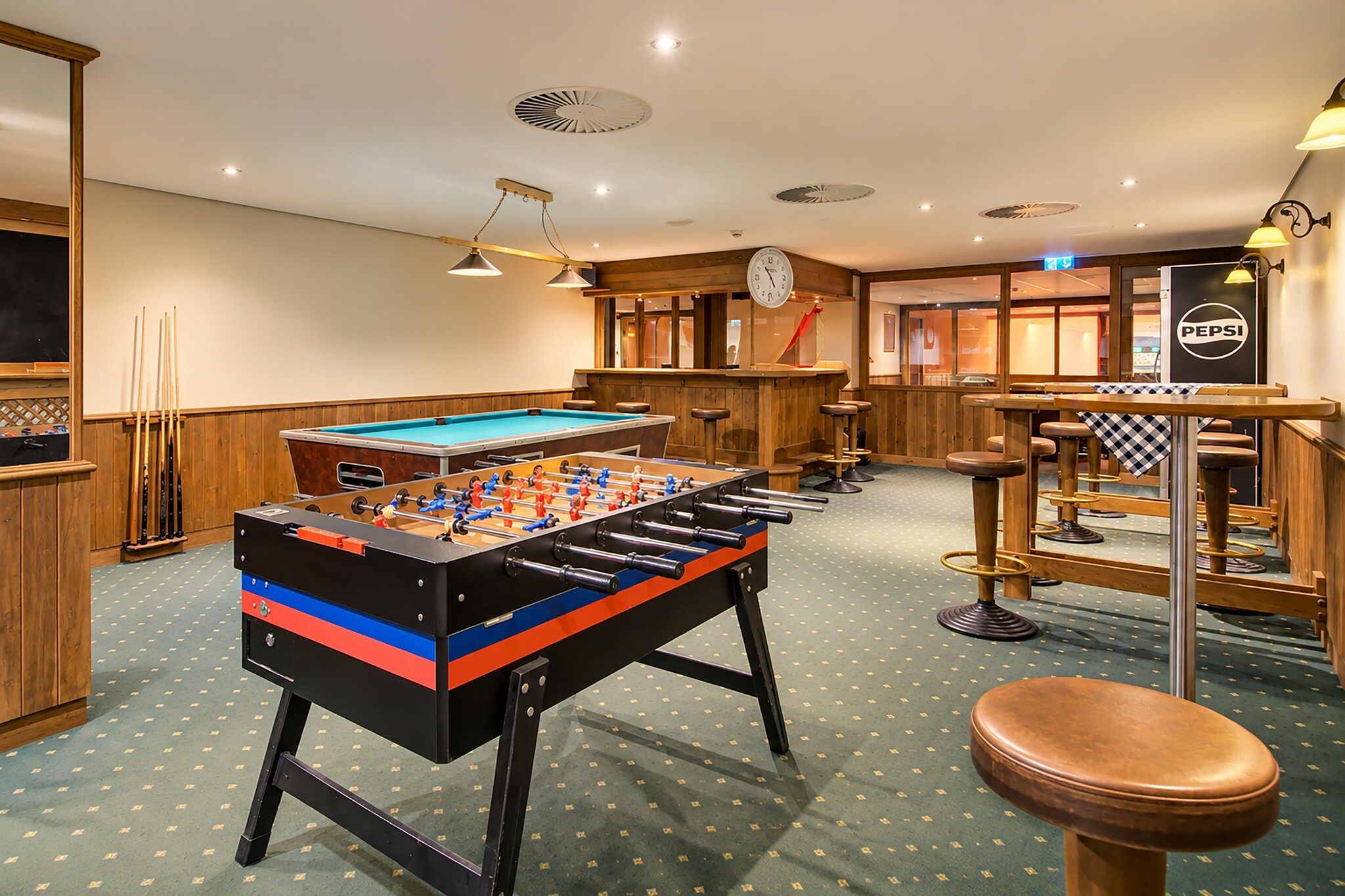 Ein Zimmer mit Kicker-, Billardtisch und einer Bar mit Hockern.