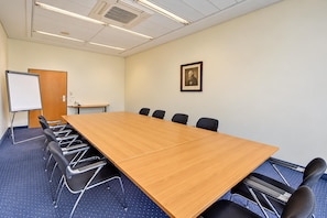 Une salle de conférence avec une longue table, des chaises, un tableau blanc et un tableau encadré accroché au mur.