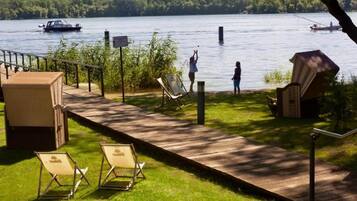 A wooden deck with lounge chairs and a covered seating area overlooking a lake with boats.