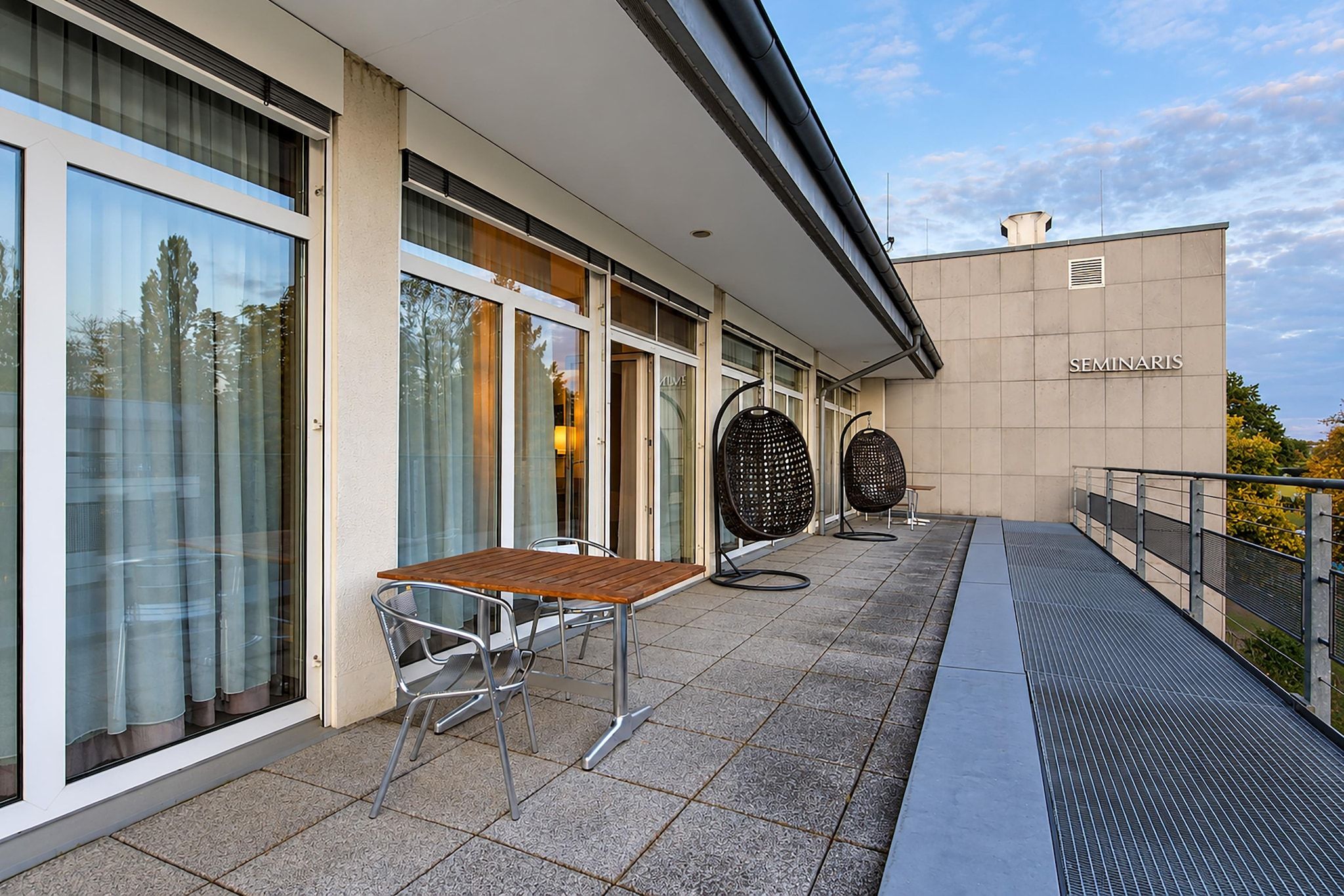 Un bâtiment moderne doté d’un espace extérieur abrité comprenant une table et des chaises, une pergola et une enseigne indiquant « SEMINARIS ».