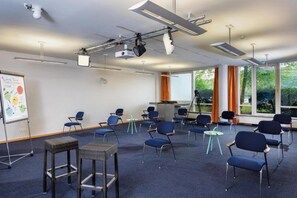 Un salón de conferencias con filas de sillas, un proyector y una pizarra.