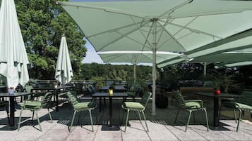 An outdoor seating area with tables and chairs, umbrellas, and a view of trees.