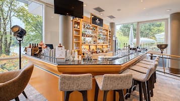 Un'area bar moderna con un lungo bancone, sgabelli da bar e un grande schermo televisivo.