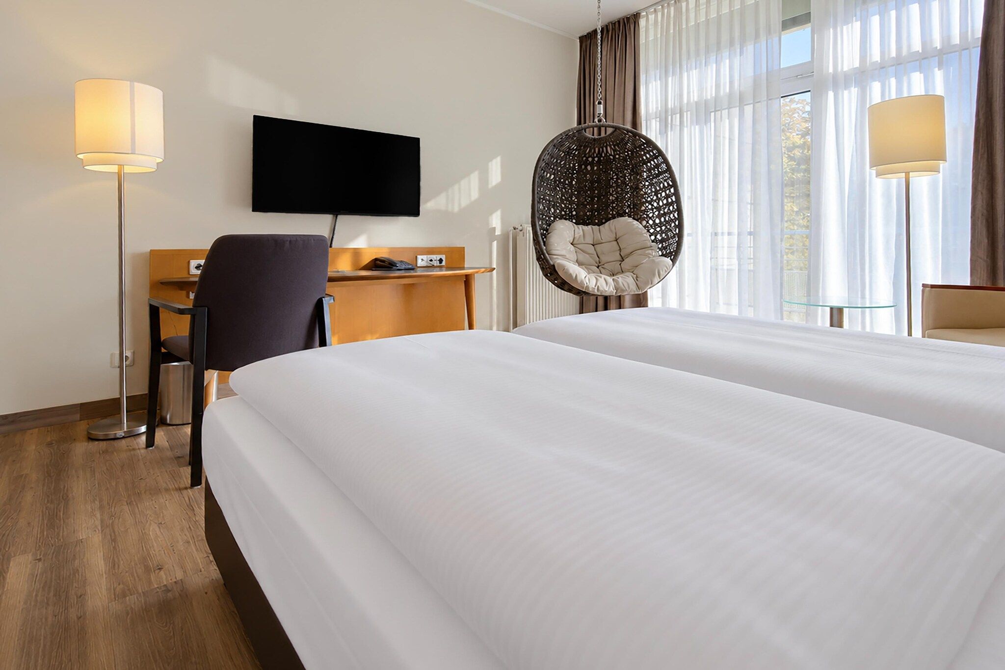 Een hotelkamer met een bed, een bureau, een stoel, een televisie en een hangstoel.