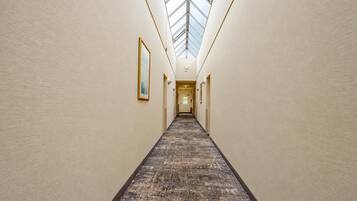 A hotel corridor with a skylight, carpeted floor, and framed artwork on the walls.