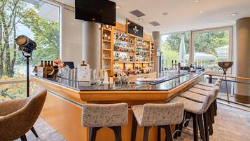 A modern bar area with a long counter, bar stools, and a large TV screen.