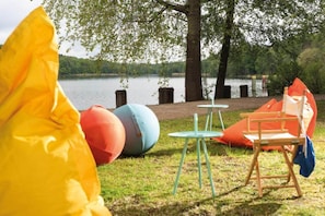 Preparación para un picnic junto al lago, con una mesa, sillas y pelotas coloridas.