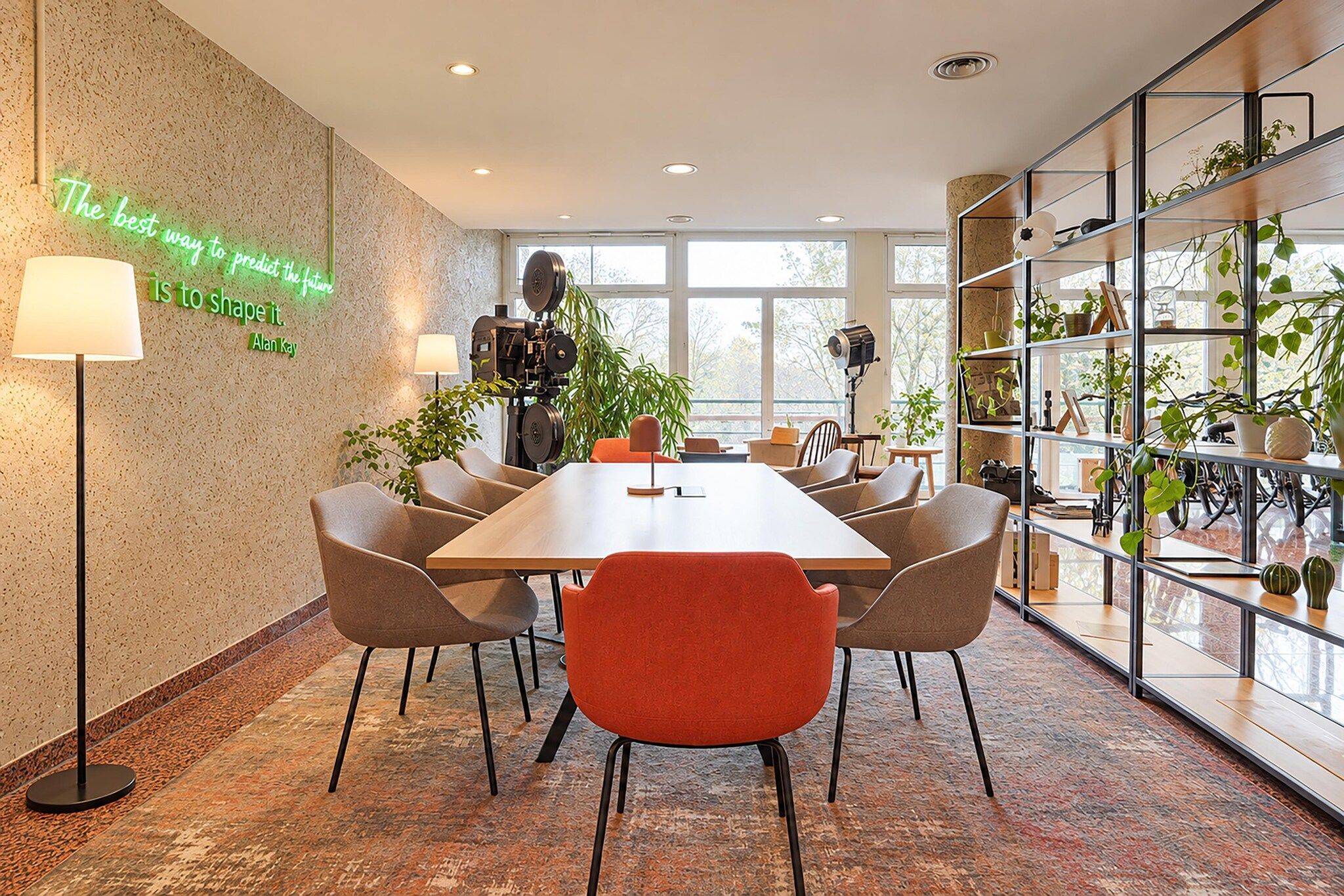 A conference room with a long table, six chairs, and a bookshelf filled with plants.