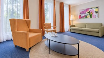 A hotel room with a blue carpet, a round table with a glass centerpiece, a sofa, two armchairs, and a painting on the wall.
