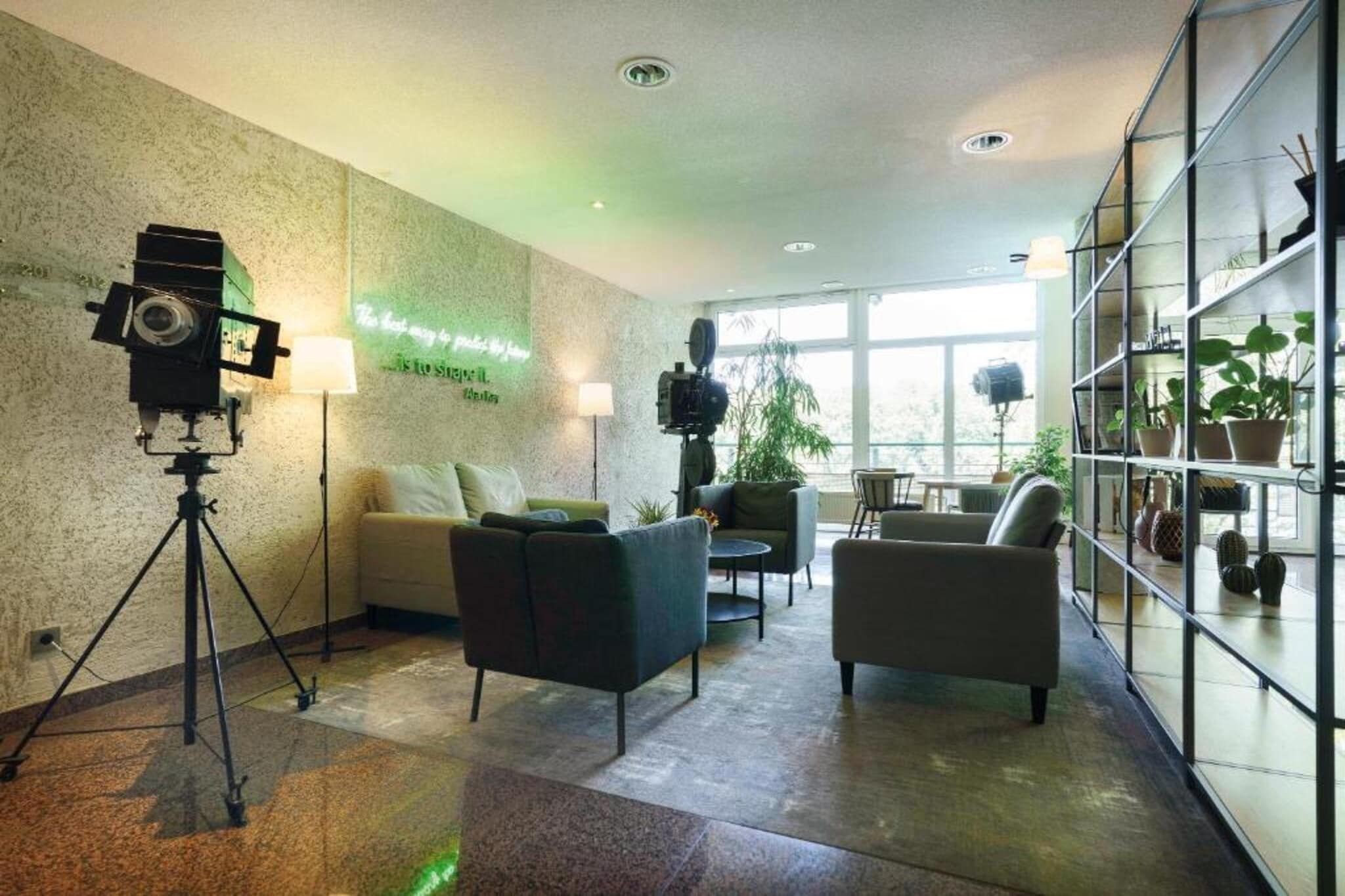 Un intérieur moderne avec un canapé, des fauteuils, un trépied et une étagère agrémentée de plantes.