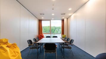 Un salón de conferencias con una larga mesa, sillas y vistas a árboles a través de amplias ventanas.