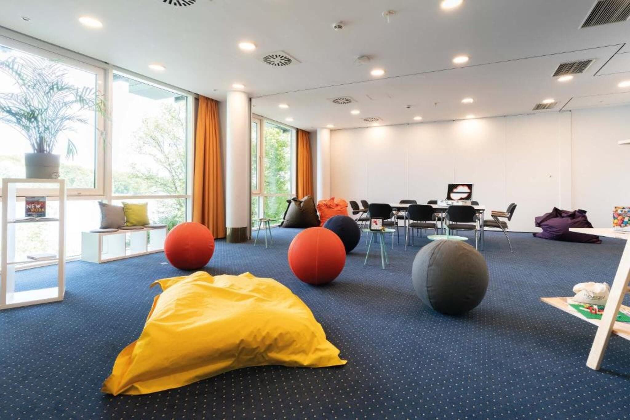 Una sala de conferencias moderna con alfombra azul, asientos redondos y un amplio ventanal con cortinas.