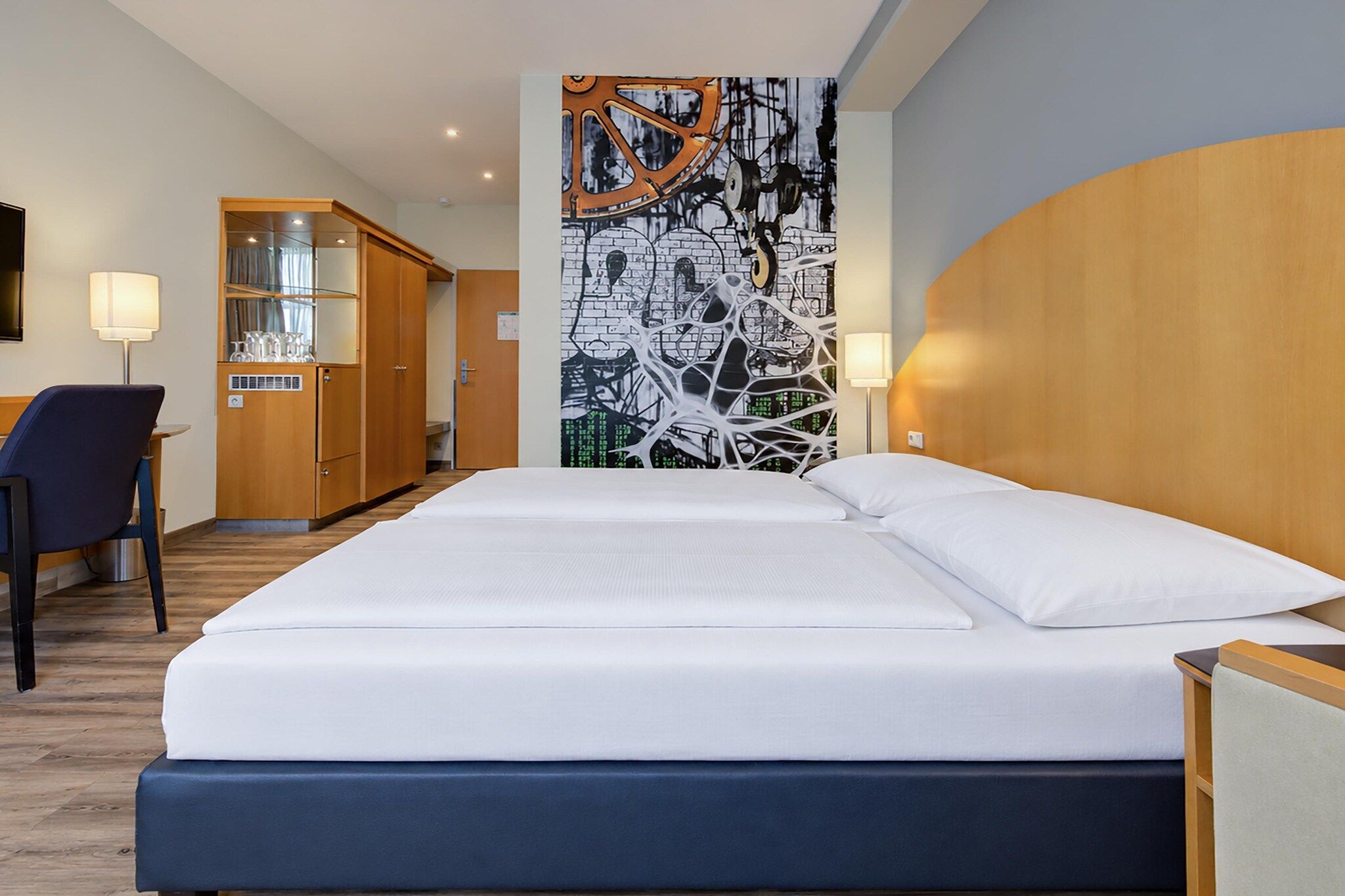 Ein Hotelzimmer mit einem Bett, einem Schreibtisch, einem Stuhl, einem Kleiderschrank und einer Wand mit einem Grafikdesign.