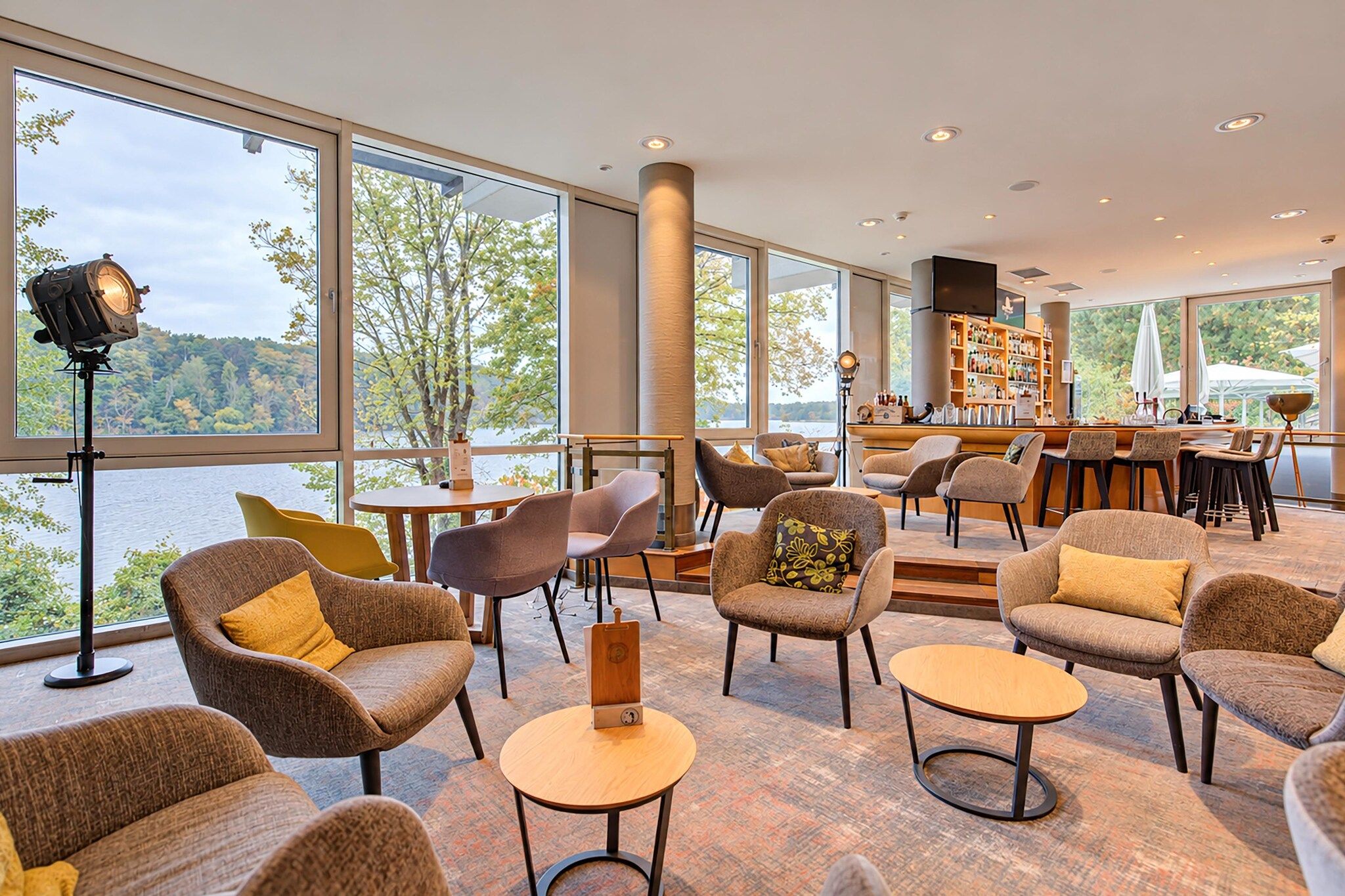 Un vaste espace intérieur aménagé avec de nombreux coins salon, de grandes fenêtres donnant sur l’extérieur et un bar avec des étagères remplies de bouteilles.