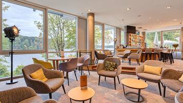 Un vaste espace intérieur aménagé avec de nombreux coins salon, de grandes fenêtres donnant sur l’extérieur et un bar avec des étagères remplies de bouteilles.