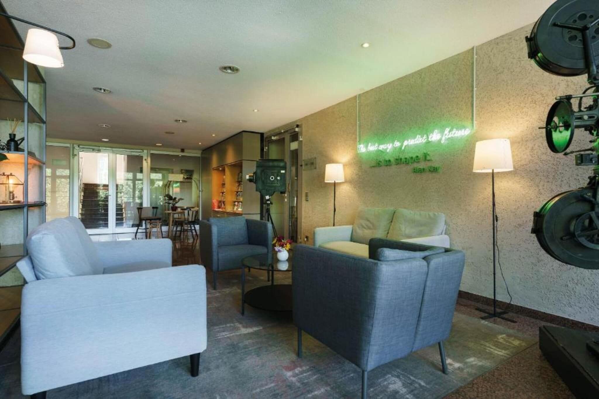 Un hall d’hôtel moderne, doté d’un espace salon avec des fauteuils, une table basse et un panneau lumineux au néon sur le mur.