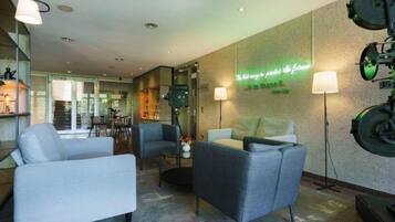 Un hall d’hôtel moderne, doté d’un espace salon avec des fauteuils, une table basse et un panneau lumineux au néon sur le mur.