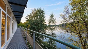 Ein modernes Gebäude mit einem überdachten Gang, der auf ein Gewässer und Bäume blickt.