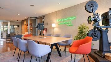 Ein moderner Konferenzraum mit Holztisch, grau-orangefarbenen Stühlen, Projektor und einem motivierenden Zitat an der Wand.