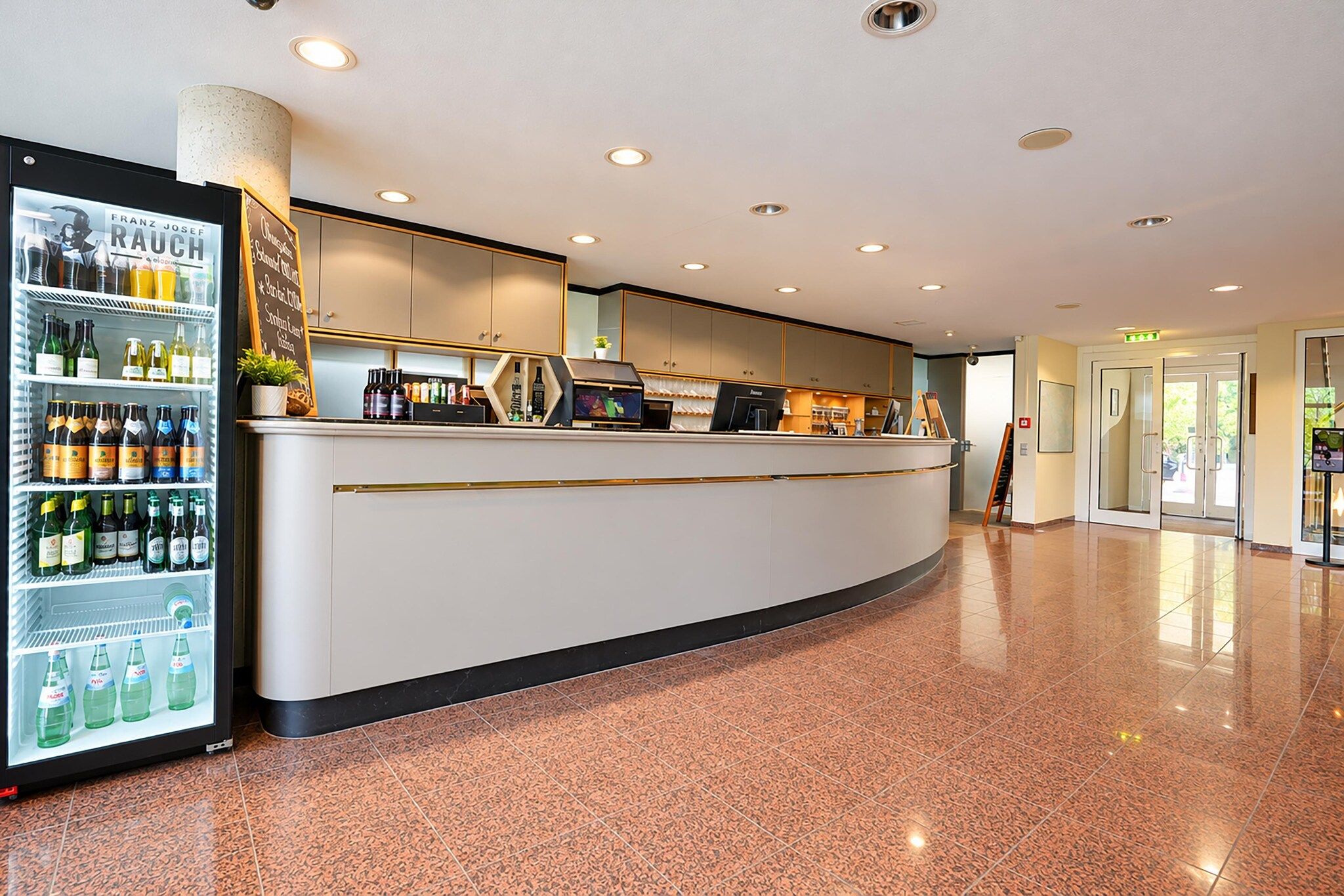 Un hall d’hôtel comprenant un comptoir d’accueil, un réfrigérateur pour les boissons et un sol carrelé.