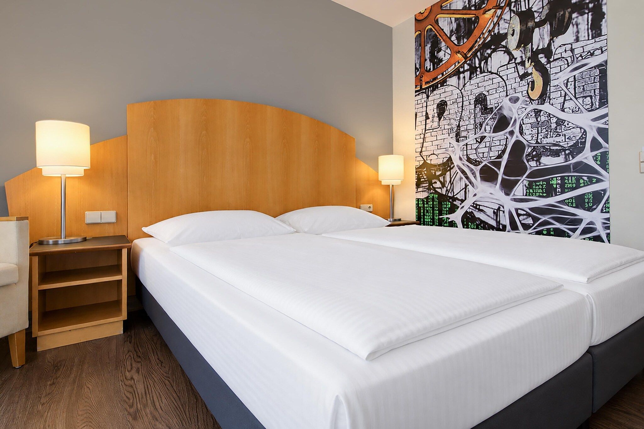 Une chambre d’hôtel avec un grand lit, deux lampes de chevet, une tête de lit en bois et un mur orné d’un motif graphique.