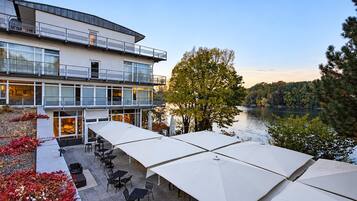 Ein modernes Gebäude mit Balkon und Seeblick, Außenbereich mit Sonnenschirmen und freier Wasseransicht.