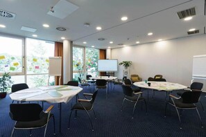 Un salón de conferencias con mesas redondas, sillas, una pantalla de proyector y ventanas con notas adhesivas.