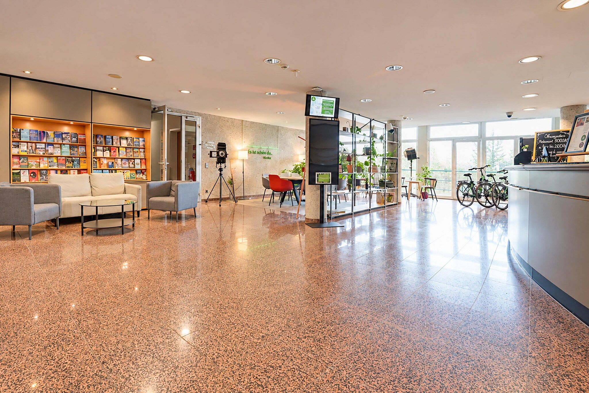 Un hall d’entrée spacieux avec un sol ciré, un coin salon, des étagères à livres, un appareil photo sur un trépied et des vélos en arrière-plan.