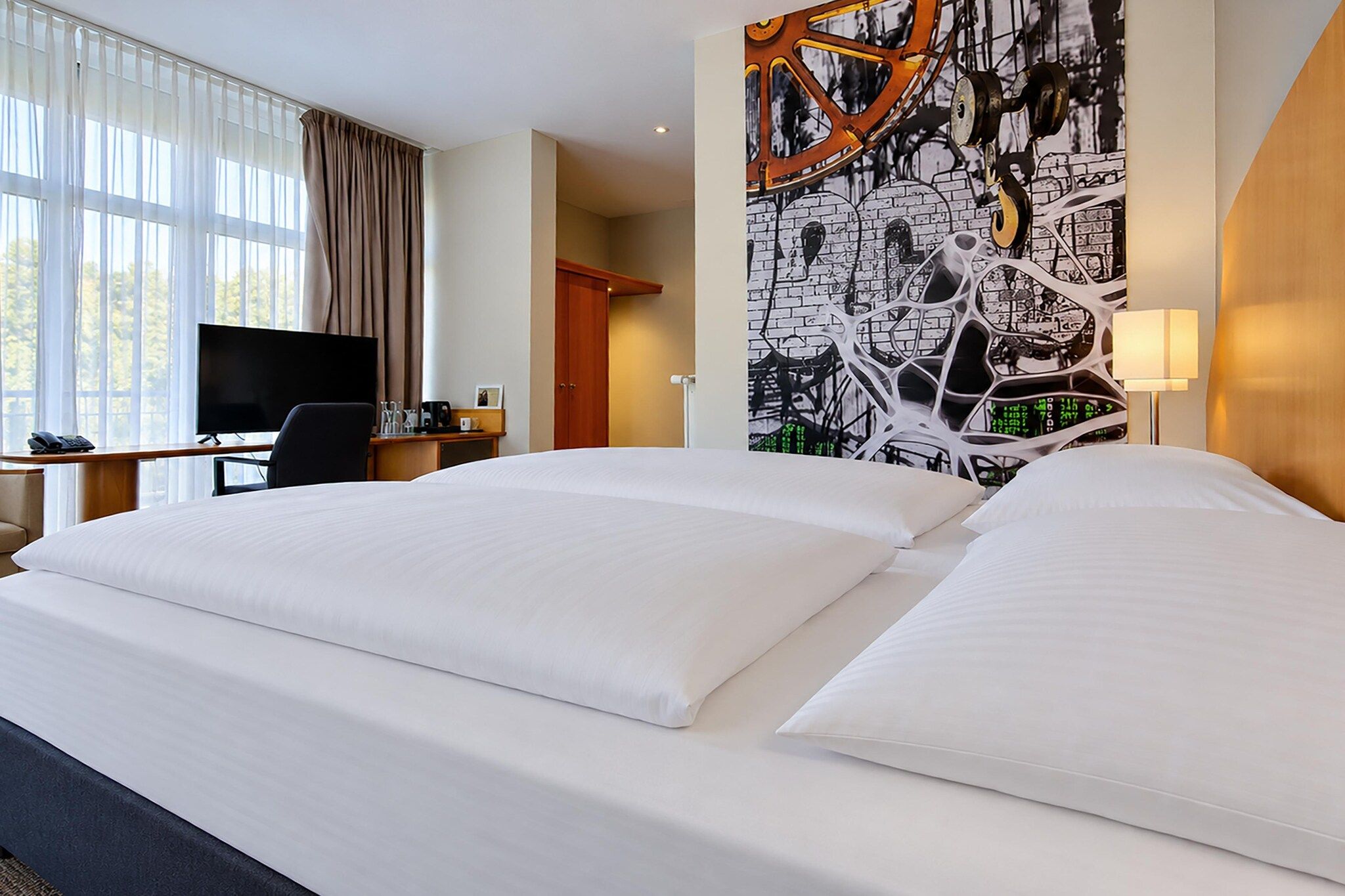 Une chambre d’hôtel avec un grand lit, un bureau avec une télévision et un mur orné d’un motif graphique.