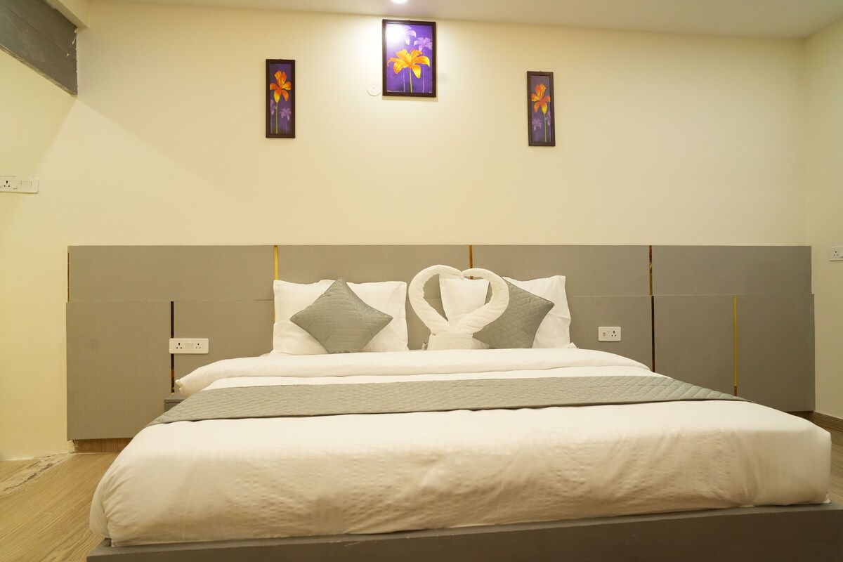 A neatly made bed with a headboard, two wall-mounted light switches, and three framed floral paintings on the wall.