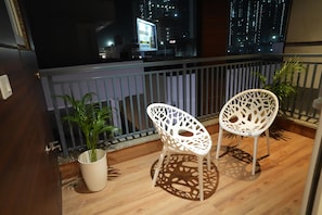 A balcony with two white chairs, a potted plant, and a view of a cityscape at night. - Hotel Elite Suites (Gurugram)