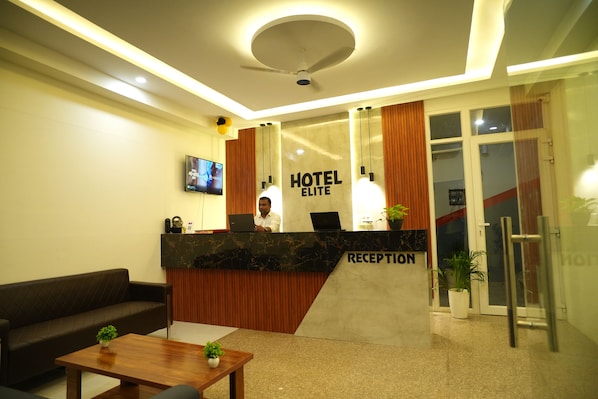 A hotel reception area with a reception desk, a sofa, a coffee table, and a television screen. - Hotel Elite Suites (Gurugram)