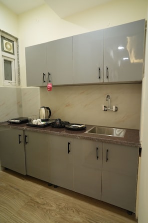 A kitchen with grey cabinets, a stainless steel sink, and a kettle on the countertop. - Hotel Elite Suites (Gurugram)