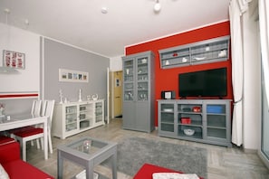 Un salon avec un téléviseur, des meubles rouges et gris, une table à manger et un canapé rouge.