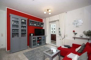 A living room with a red sofa, a grey cabinet, a flat-screen TV, and a glass coffee table. - Holiday apartment with 1 bedroom (Seebad Heringsdorf)