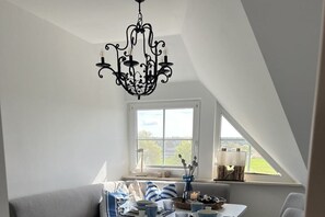 A dining area with a chandelier, a table set with dishes, and a view of the outdoors through a window. - Apartments Ostseesonne (Sellin\/Moritzdorf auf Rügen)