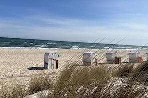 A beach with sand, ocean waves, and beach huts labeled with numbers. - Apartments Ostseesonne (Sellin\/Moritzdorf auf Rügen)