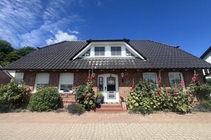 A two-story house with a brick facade, a tiled roof, and a front porch with steps leading to a door. - Apartments Ostseesonne (Sellin\/Moritzdorf auf Rügen)