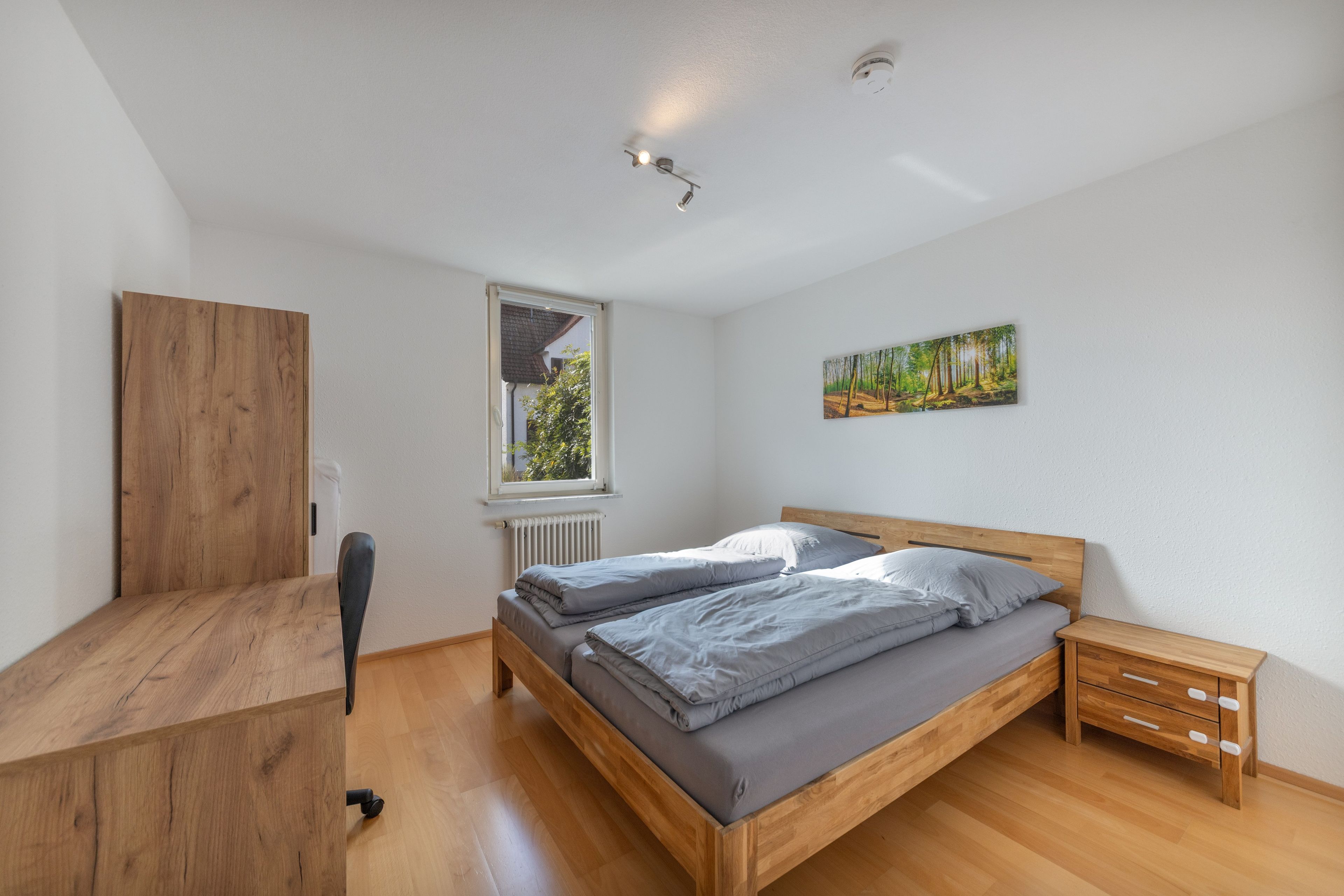 A bedroom with a wooden bed, a radiator, a window, and a painting on the wall.