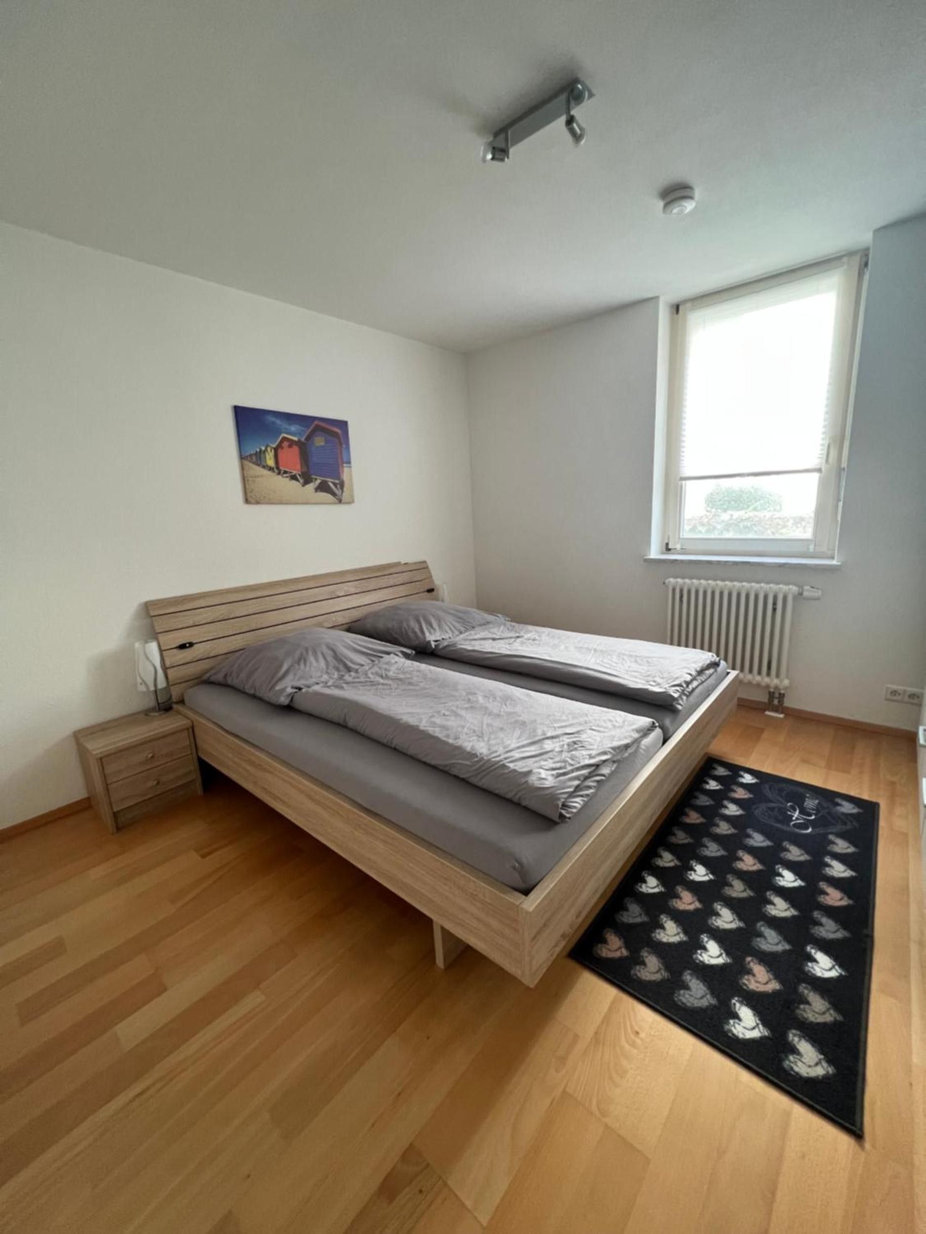 Une chambre à coucher avec un lit en bois, une table de chevet, un radiateur et une fenêtre.