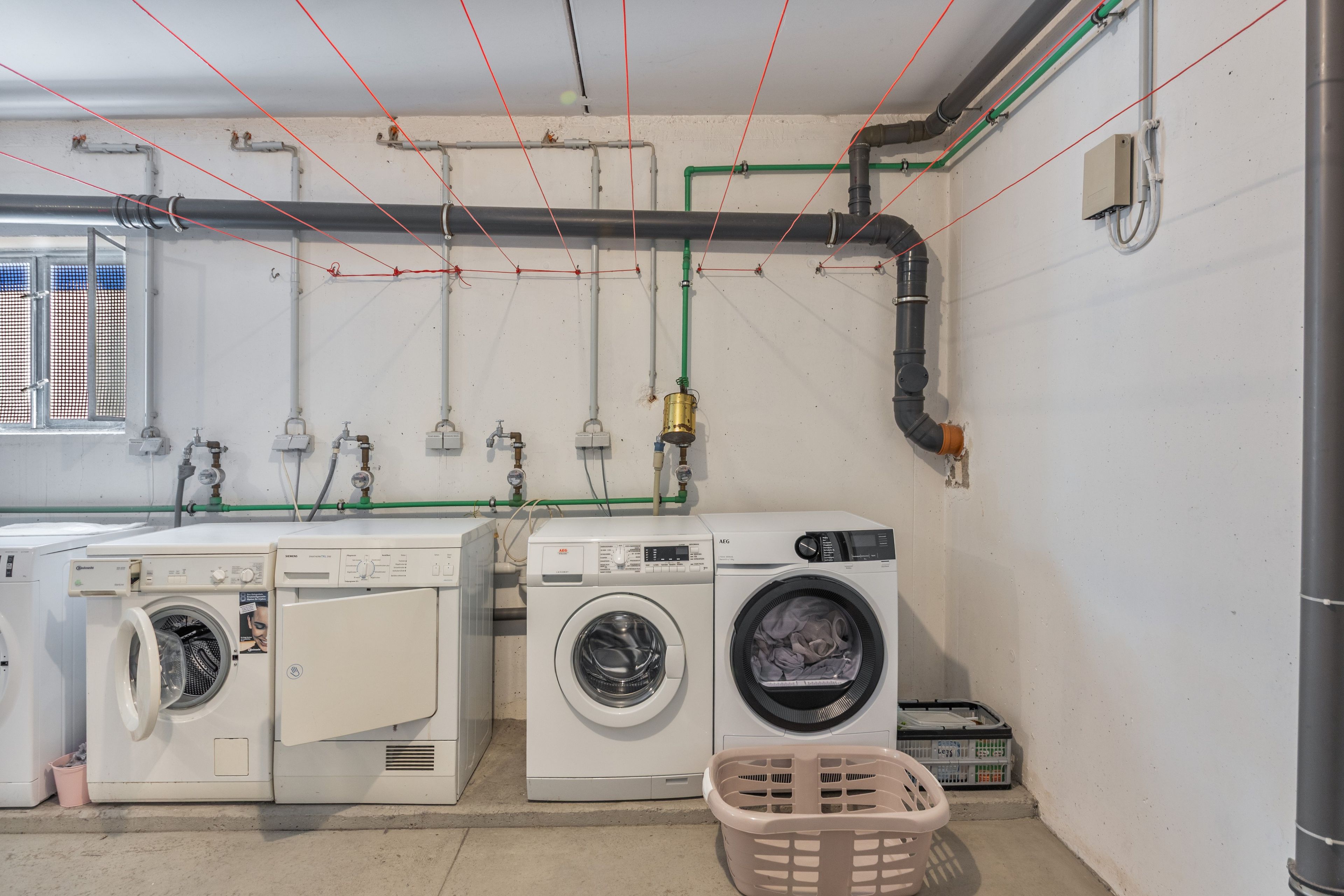 Una sala de bugaderia amb dues rentadores, un assecador i diverses canonades i mànegues.