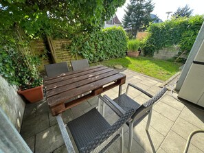 Eine Außenpatio mit Holztisch und -stühlen, umgeben von Grünpflanzen und einer Backsteinmauer.