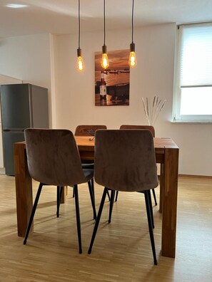Un comedor con una mesa de madera y cuatro sillas, una lámpara colgante y un refrigerador al fondo.
