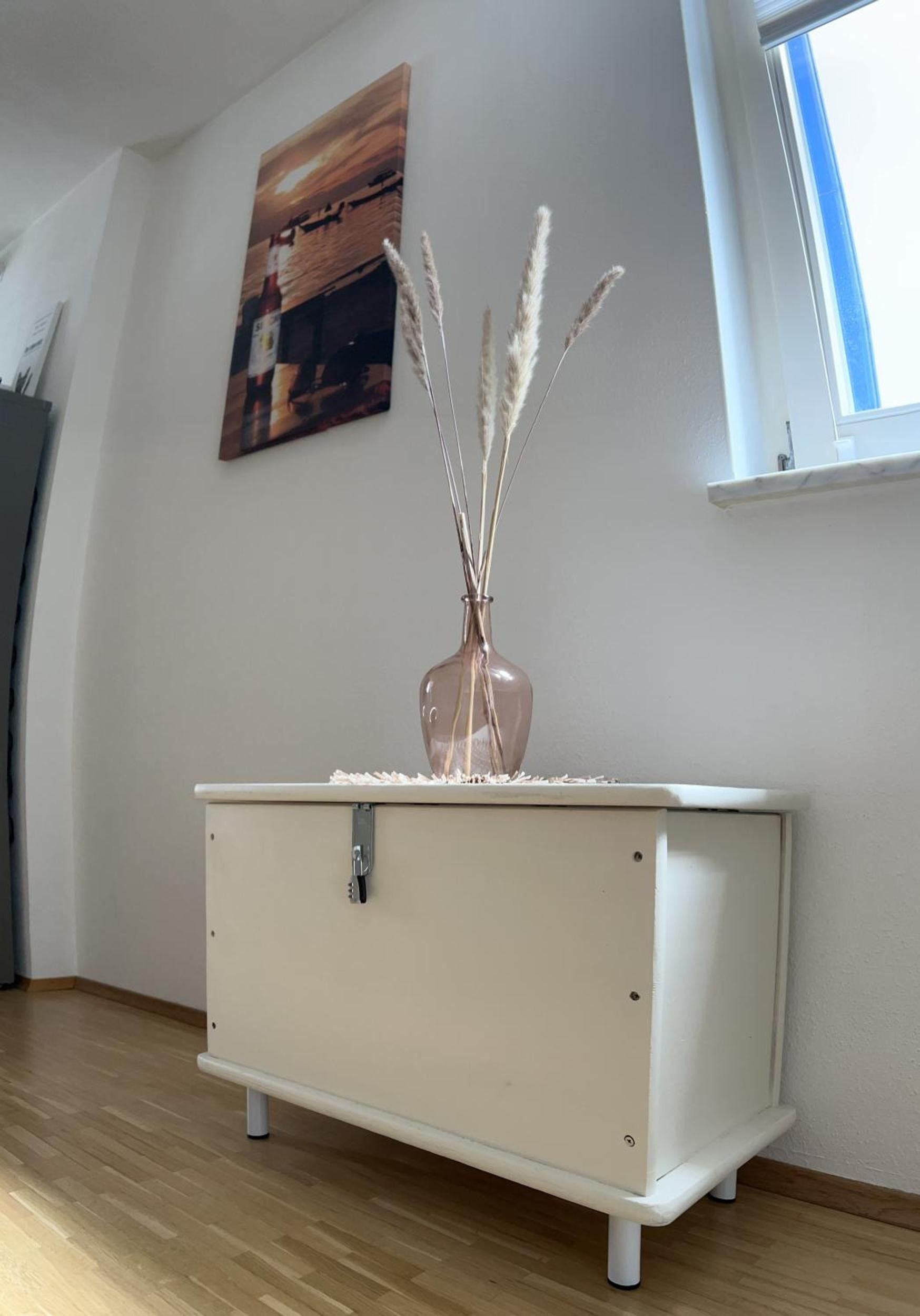 Una habitación con un tocador blanco, un cuadro en la pared y una ventana.