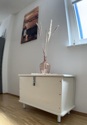 Una habitación con un tocador blanco, un cuadro en la pared y una ventana.