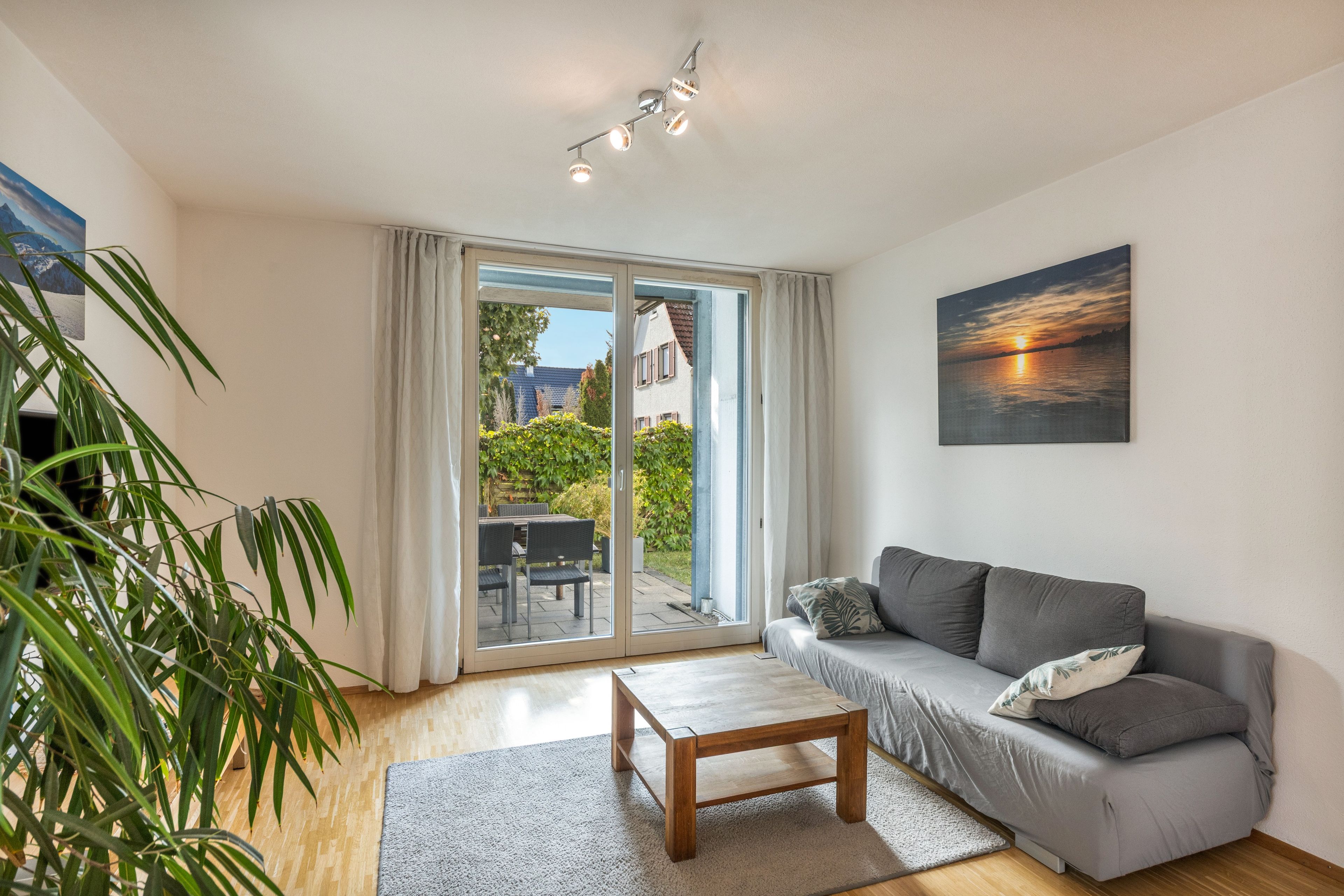 A modern living room with a grey sofa, a wooden coffee table, and a large window with curtains.