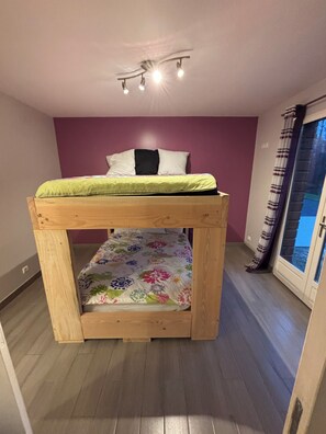 Una cama individual superpuesta con una colcha estampada, una pared morada y una ventana con cortinas.