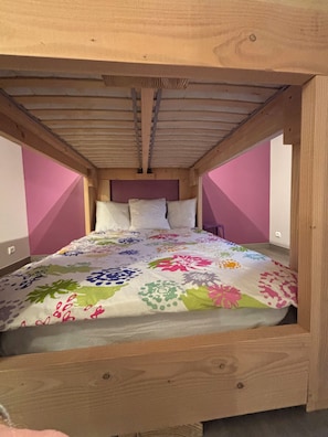 A wooden bed with a colorful floral bedspread in a room with pink walls and a sloped ceiling.