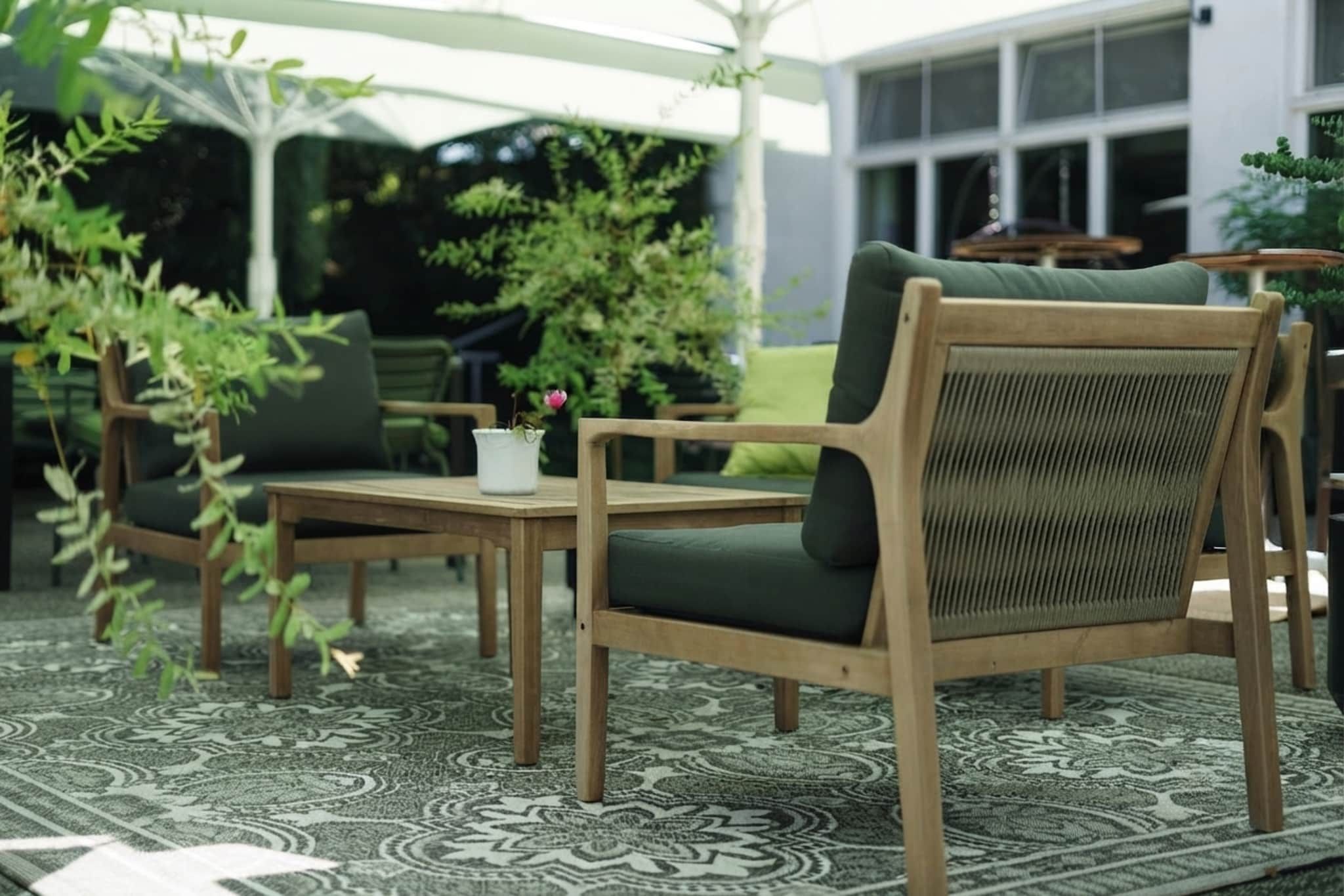 Un área de estar exterior con mobiliario de madera y un tapete estampado.